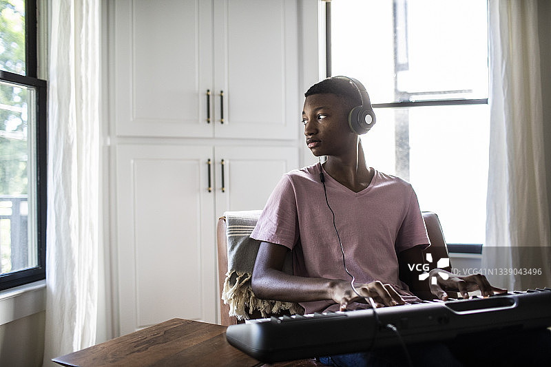 戴着耳机在家弹键盘的少年图片素材