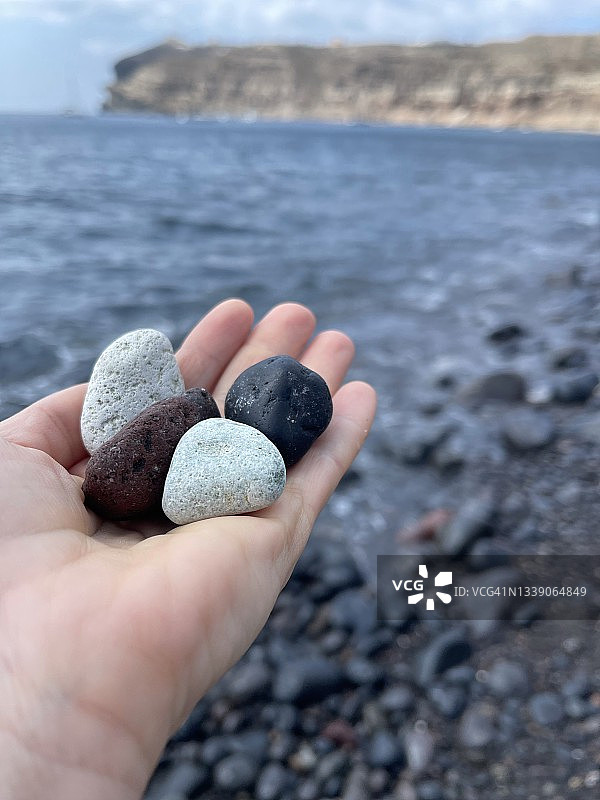 手持鹅卵石，希腊圣托里尼阿克罗蒂里白色海滩特写图片素材