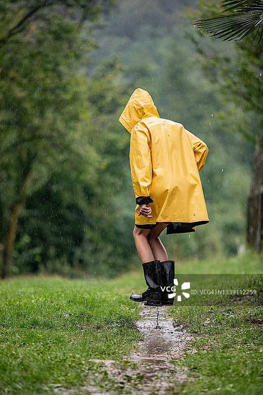 成年女性穿着雨衣和橡胶靴在雨中泥坑里跳跃图片素材