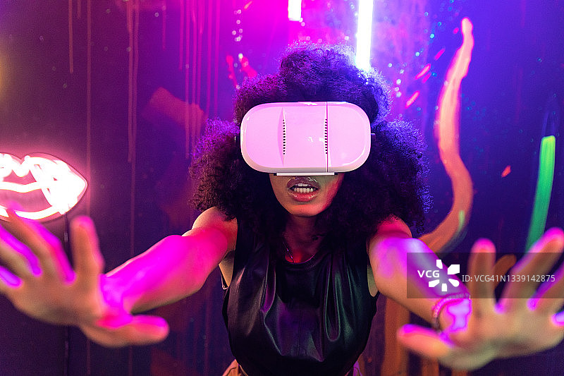 震惊的女性戴着VR眼镜在霓虹灯工作室体验网络空间图片素材