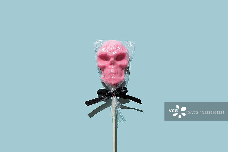 蓝色背景上的骷髅头粉色棒棒糖，万圣节主题图片素材