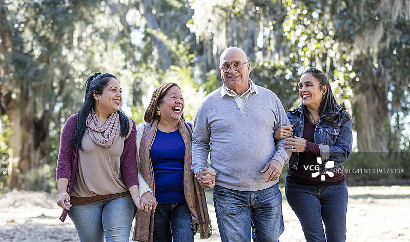 与成年女儿在公园散步的年长西班牙裔夫妇图片素材