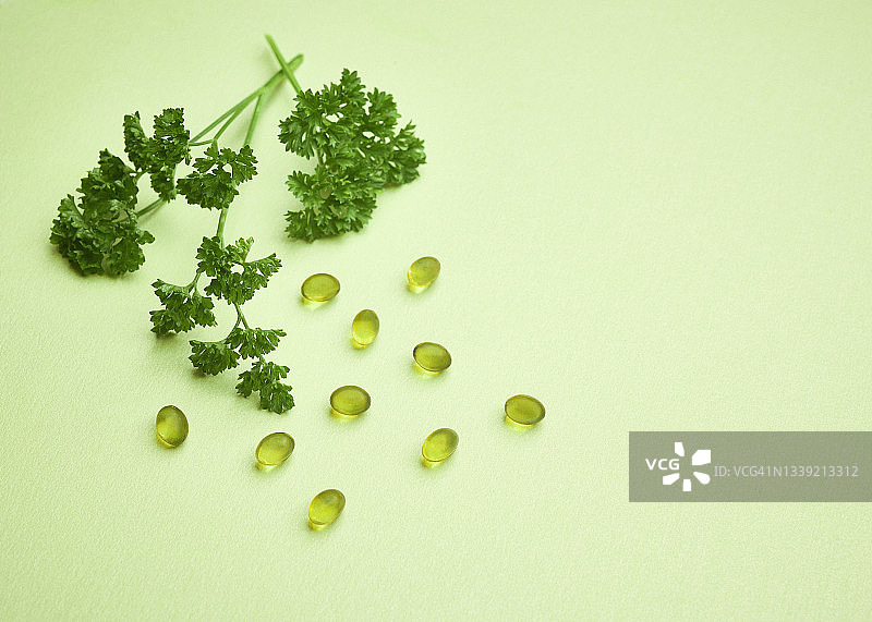 绿色纸背景上的欧芹和透明明胶营养补充剂胶囊图片素材