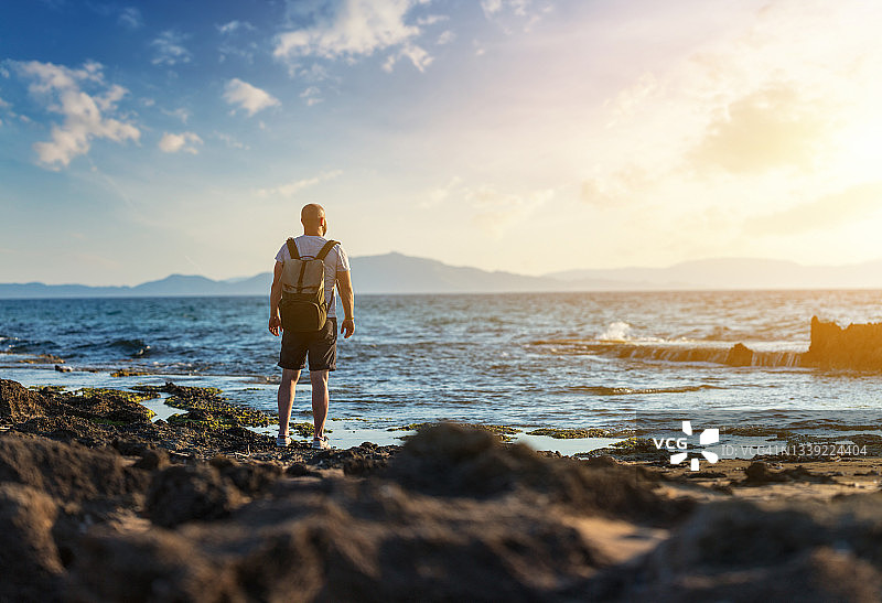 独自站在日落时多岩石海滩上的男人图片素材