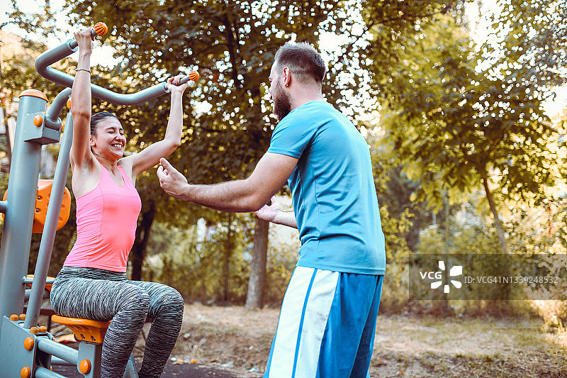 男性健身教练帮助女性在户外健身器材上取得更好成绩图片素材