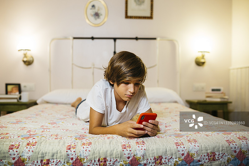 在床上使用智能手机的男孩图片素材