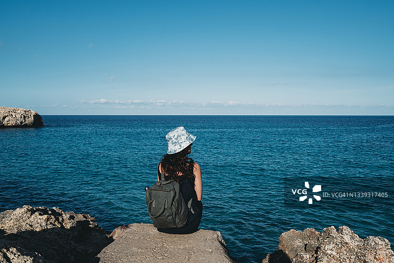 一名女子戴着渔夫帽，坐在海边的岩石上图片素材