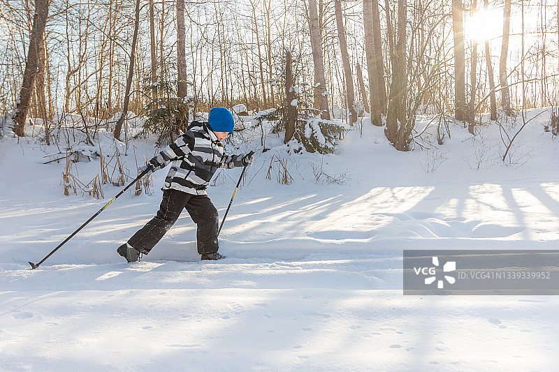雪地冬季景观中进行越野滑雪的运动小男孩，逆光拍摄图片素材