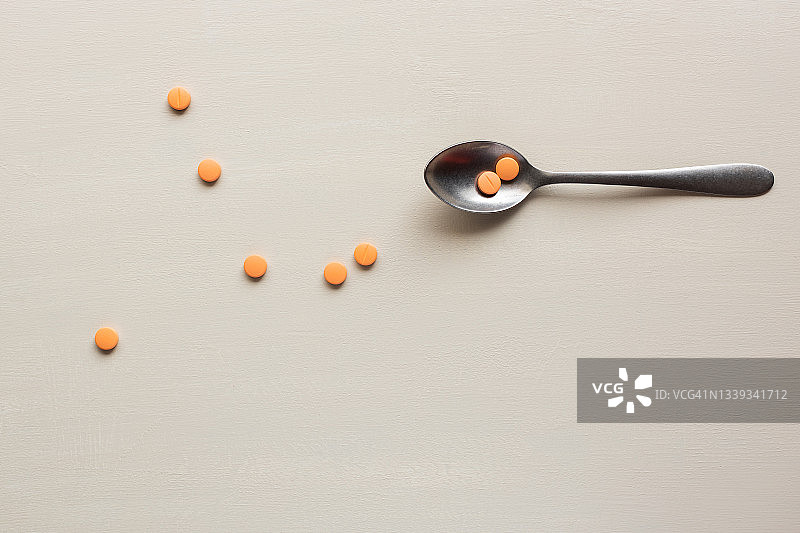 木桌上勺子里的橙色药丸俯视图图片素材