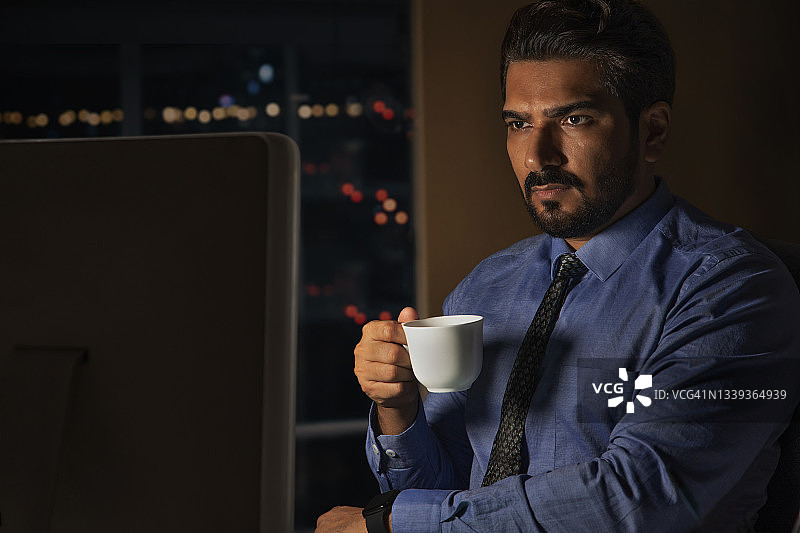 一名员工在办公室夜晚工作，手持咖啡杯，神情专注图片素材