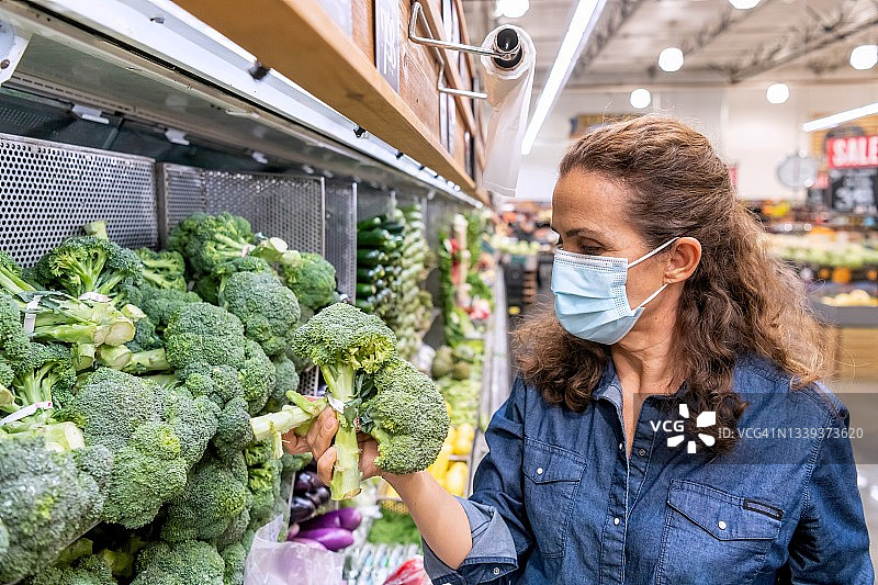 戴着防护口罩在超市购买有机蔬菜的中年妇女图片素材