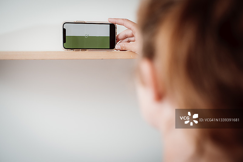 女人用智能手机当水平仪安装DIY搁架图片素材