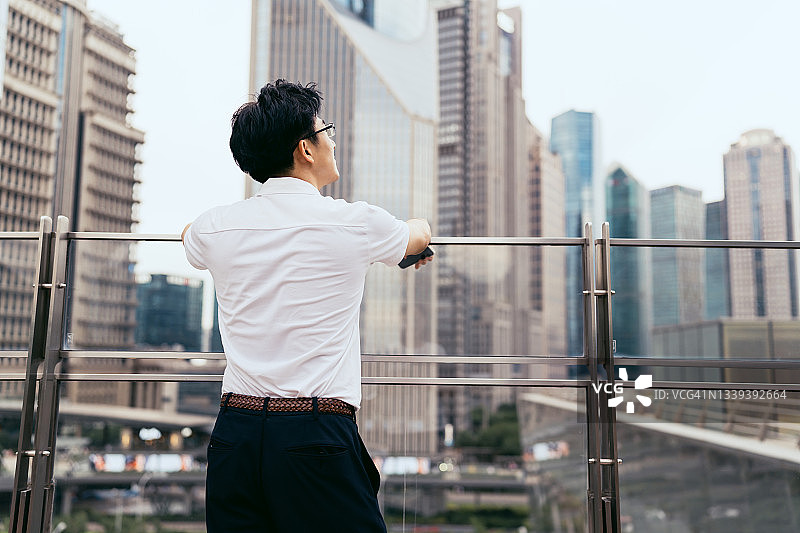 亚洲年轻商人眺望金融区城市天际线，商务出行概念图片素材