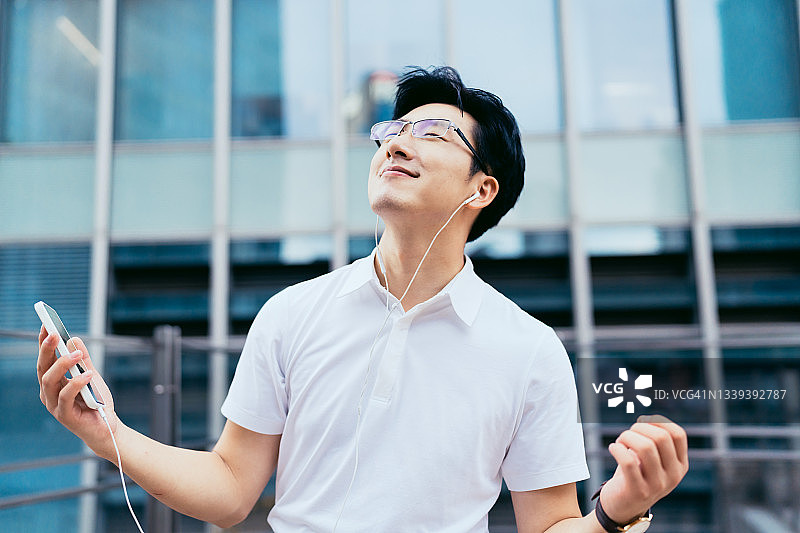 年轻的亚洲商人在金融区用智能手机戴着耳机听音乐图片素材