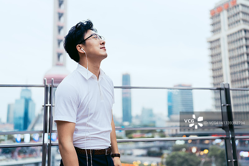 年轻的亚洲商人在金融区用智能手机戴着耳机听音乐图片素材