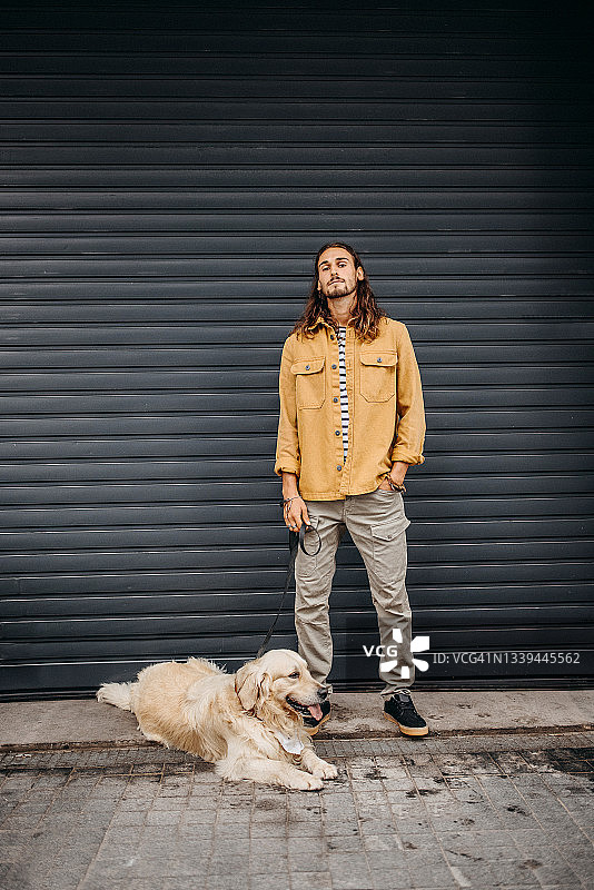 在黑色背景前与狗合影的年轻时尚男子图片素材