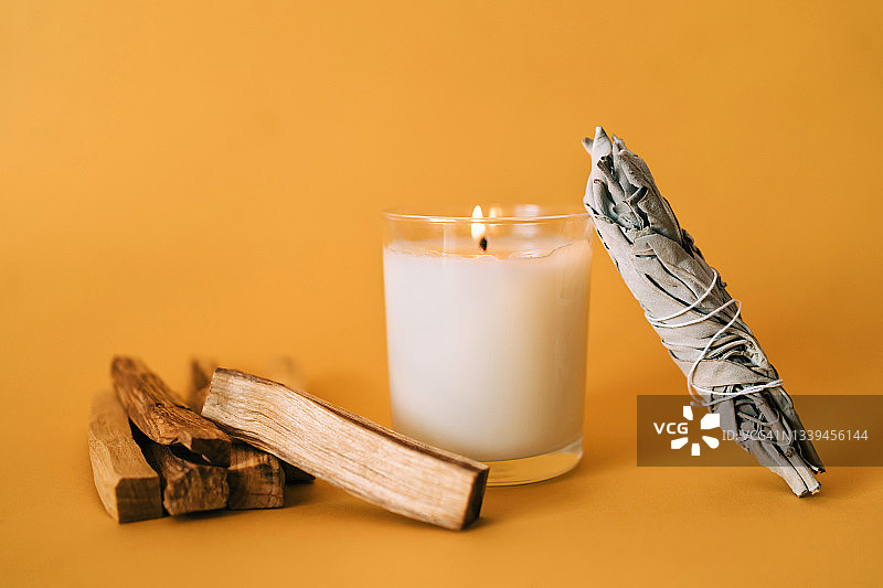 黄色背景上的圣木条、燃烧的蜡烛和白鼠尾草——芳香疗法和仪式套装图片素材