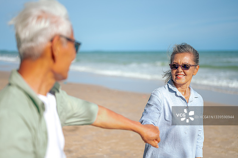 老年夫妇在沙滩上手牵手散步，享受幸福退休生活图片素材