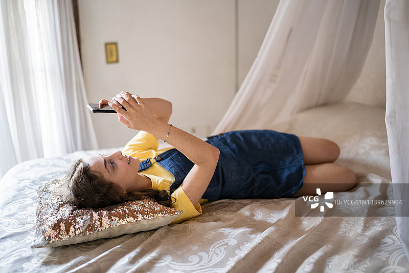 快乐的少女躺在床上用智能手机发短信图片素材