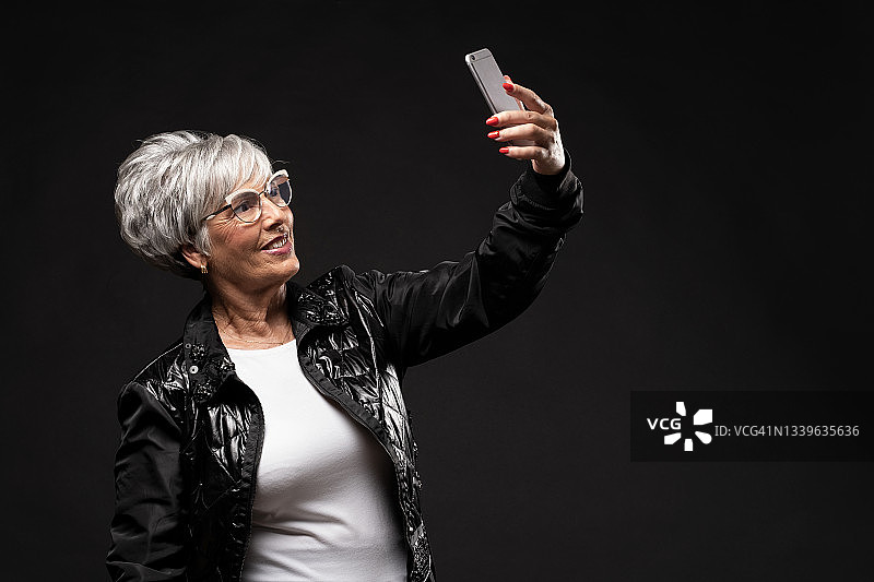 白发中年妇女用智能手机自拍肖像图片素材
