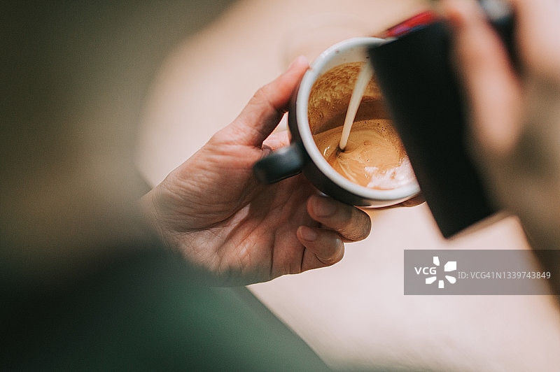 亚洲咖啡师在咖啡杯上倾倒奶泡图片素材
