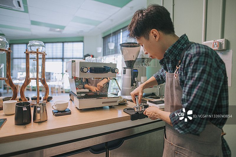 华人男咖啡师用填压器压制研磨咖啡图片素材
