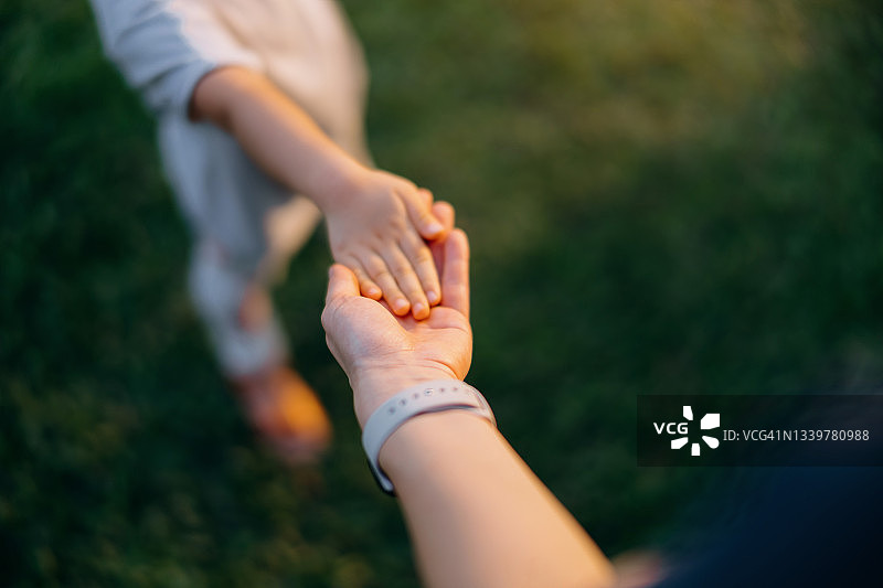 母亲在草坪上牵着小女儿的手的特写，在公园里一个美好的日子里放松并享受家庭 bonding 时光。家庭爱和关怀。与自然连接的概念图片素材