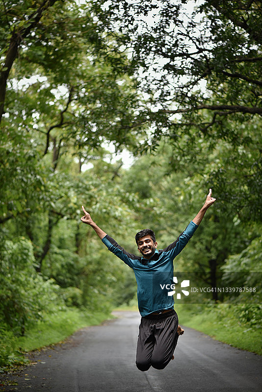 在绿树成荫的美丽道路上跳跃的年轻男人图片素材