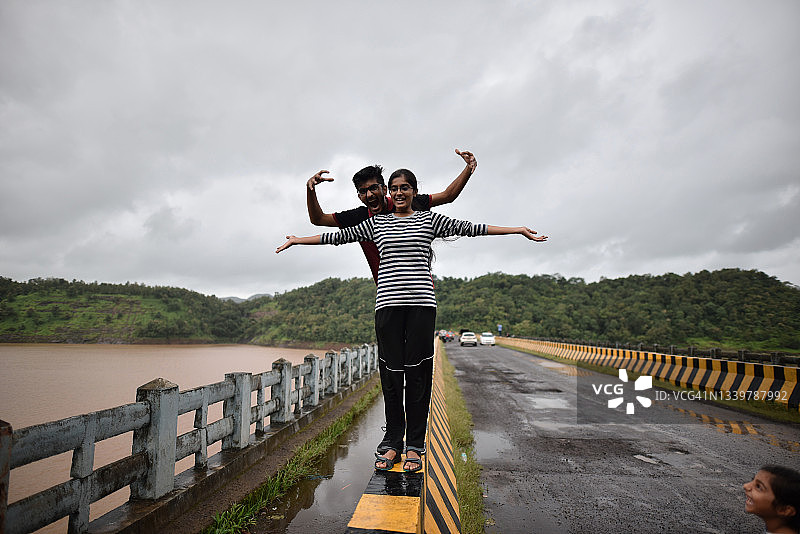 年轻男人和女人站在桥的栏杆上，周围环绕着宁静的湖面图片素材