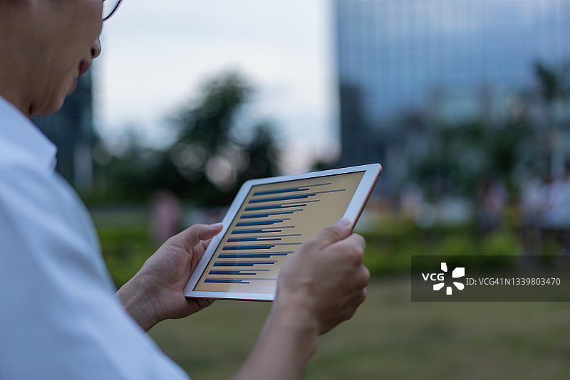 亚洲男性白领在办公楼外草地上使用平板电脑图片素材