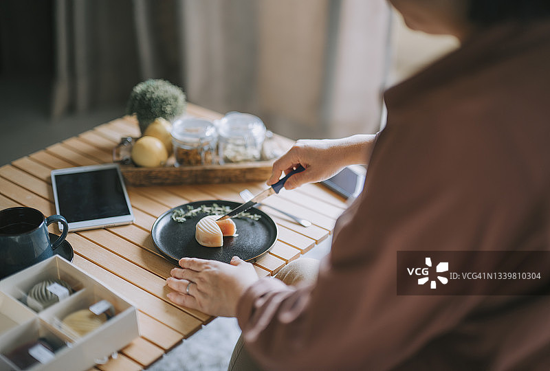 华人女性在客厅享用下午茶和中国传统节日甜点，切雪皮月饼图片素材