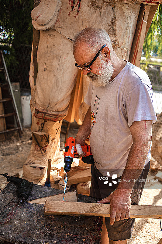 年长的艺术家使用钻孔工具制作木制雕像图片素材