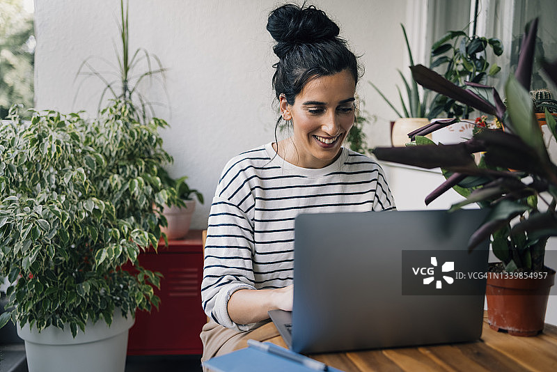 在家工作的美女，坐在阳台上用笔记本电脑打字图片素材