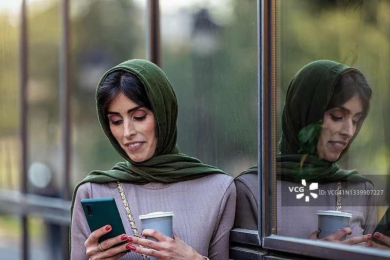 中年阿拉伯妇女在街头使用手机喝咖啡的肖像图片素材