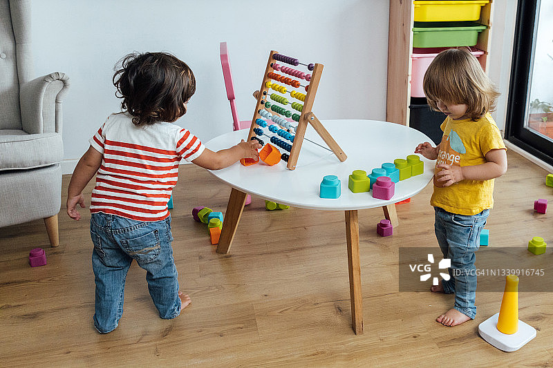 2岁儿童玩积木和塑料环，小女孩在家玩算盘的侧面图图片素材