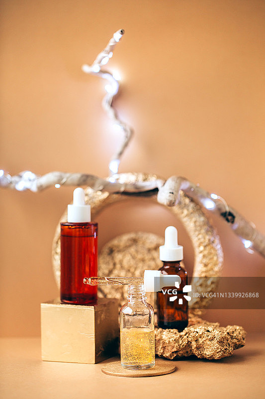 米色背景下，金色展台上玻璃瓶与滴管图片素材