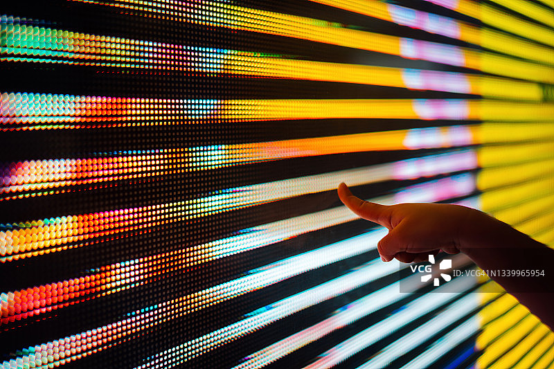 孩子的手触摸发光的多彩LED显示屏，连接未来图片素材