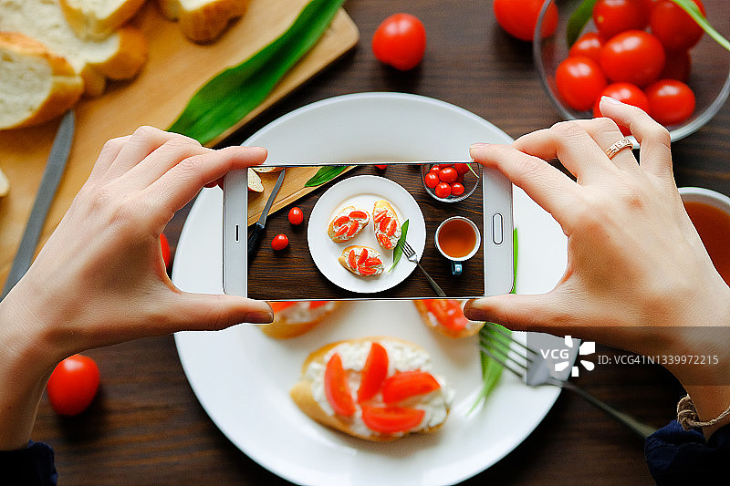 博主女孩用手机拍摄早餐的手部特写，健康农产品三明治，美食博主图片素材