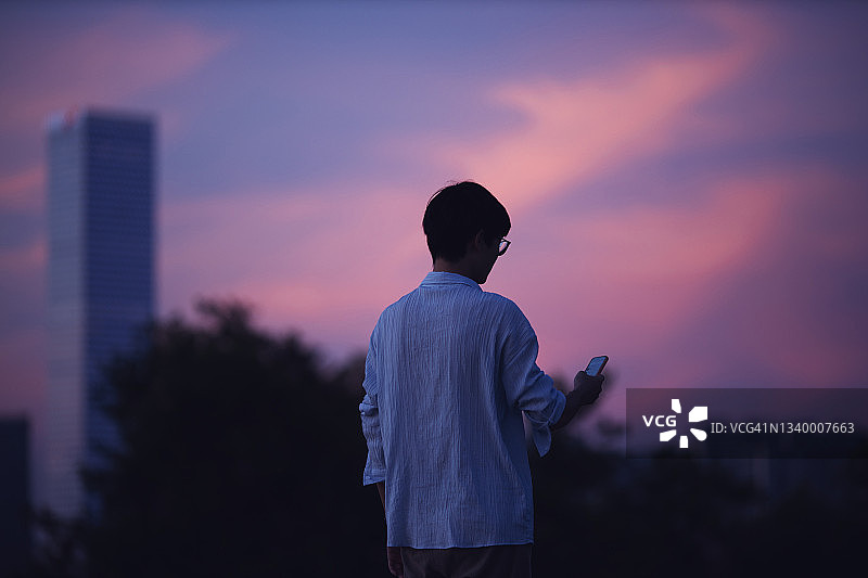 商务男士在黄昏时使用智能手机的背面视角图片素材