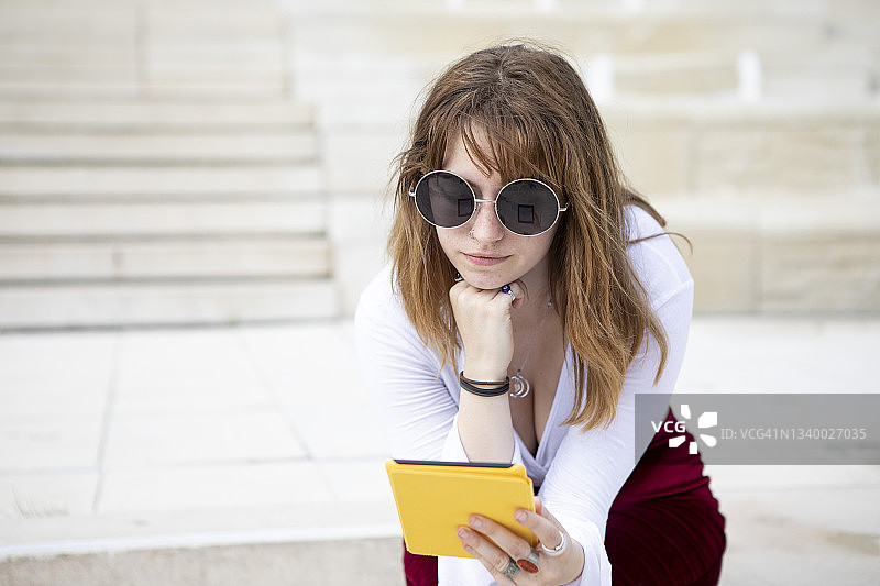 年轻女子坐在石阶上，在户外夏天使用电子阅读器图片素材