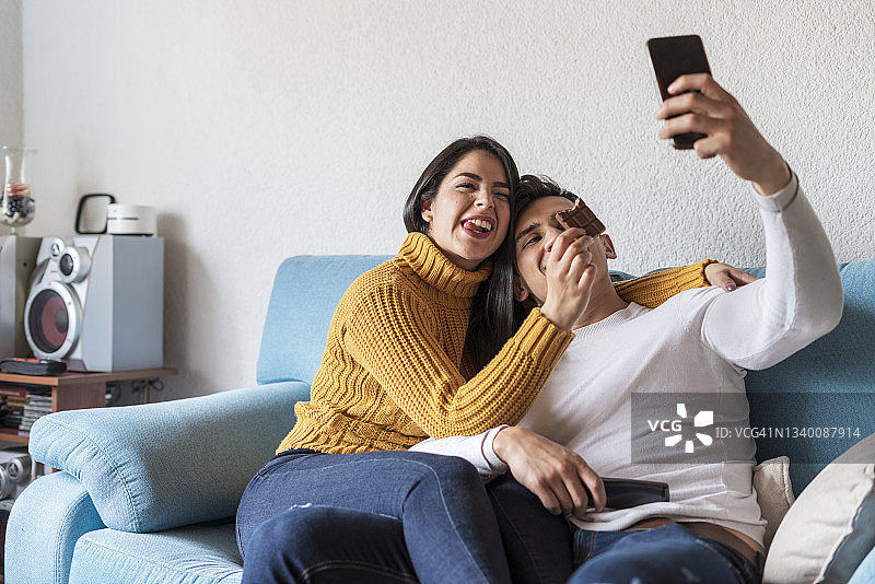 拉丁裔夫妇在客厅的沙发上自拍并吃巧克力图片素材