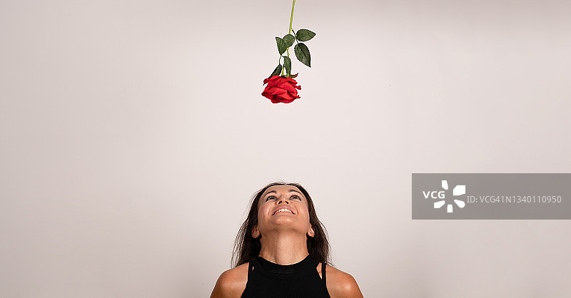 在白色背景下，年轻的女孩面带微笑，抬头看着玫瑰图片素材