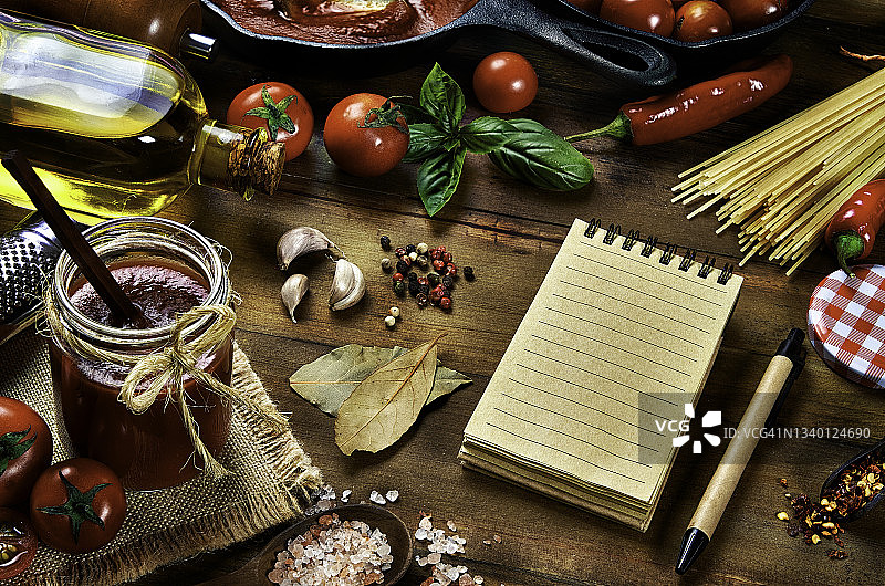 在简朴的家庭厨房中，准备意大利面和番茄酱的食材的高角度视图，配有笔记本和笔图片素材