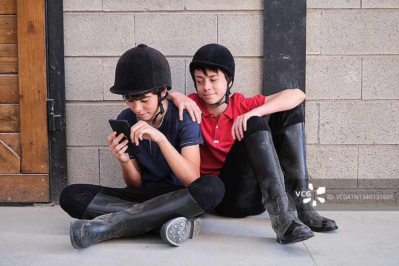 戴骑马头盔的青少年坐着玩手机图片素材