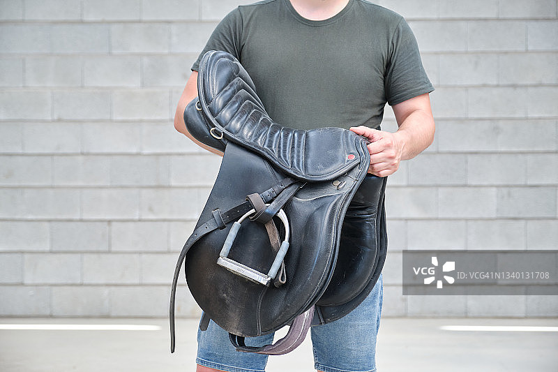 拿着马鞍的男子，背景是灰色砖墙图片素材