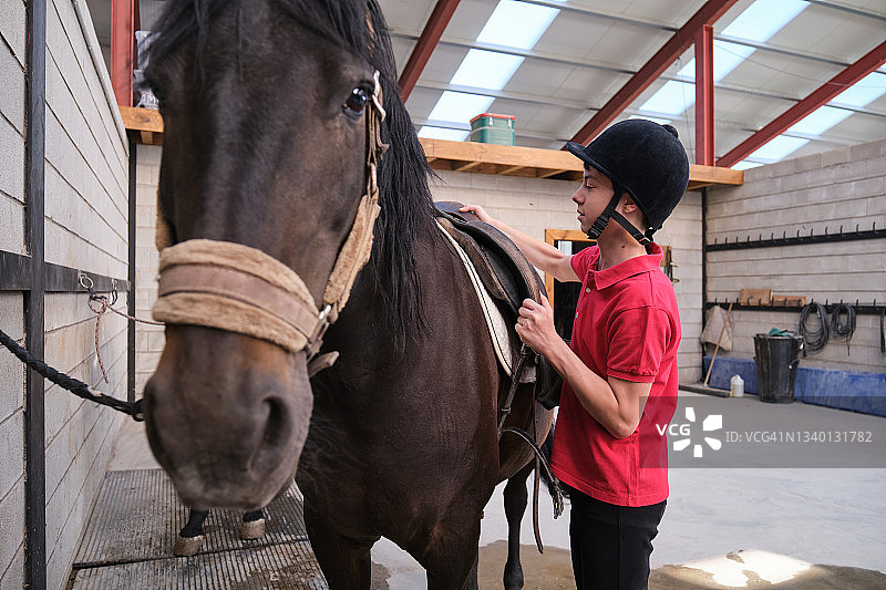 年轻骑师在骑马前给马装鞍图片素材