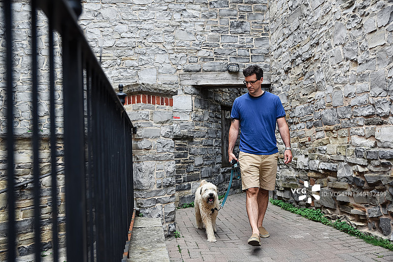 白人男子牵着蓬松的狗穿过石头小巷图片素材