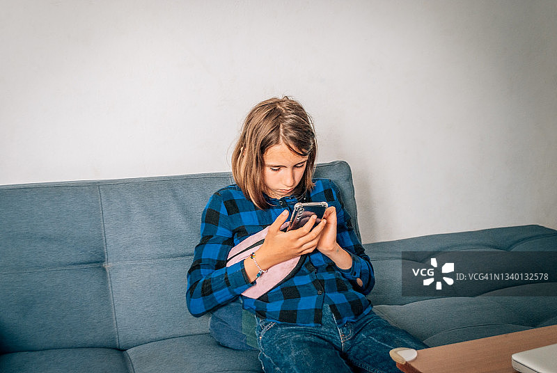 女孩在家中坐在沙发上，手里拿着手机。图片素材
