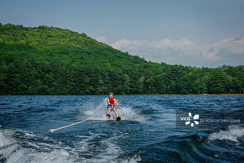 在湖上滑水，远处有绿山的青少年男孩图片素材