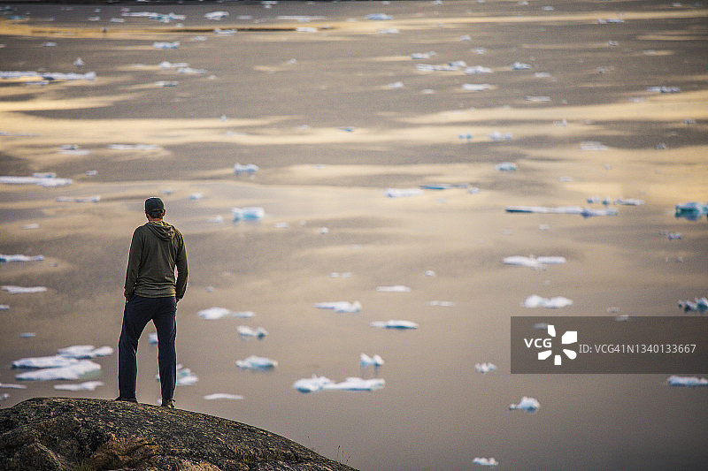 站在海洋和冰山之上的悬崖上的男子背影图片素材